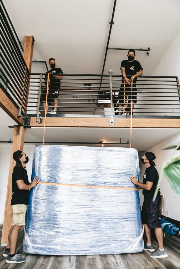 professional movers Lower Kabete - Two professional movers carry a large wrapped item outdoors.